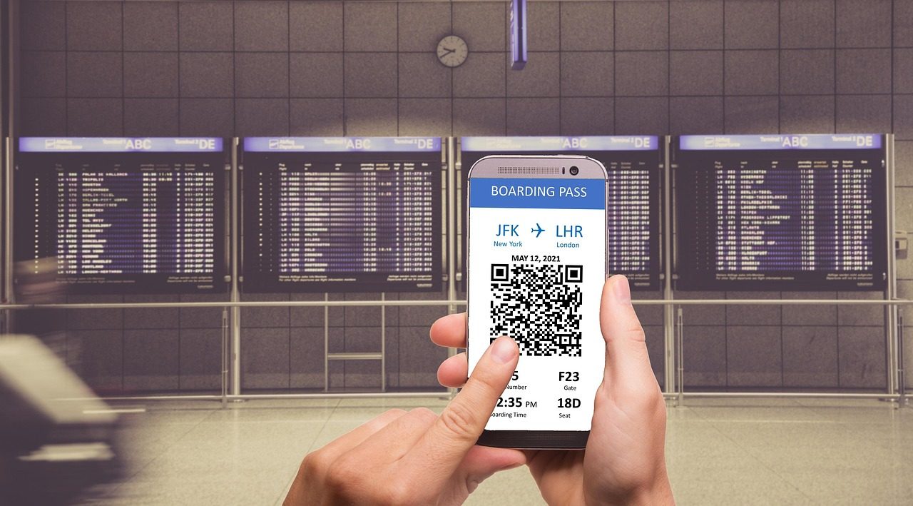 Passageiro conferindo cartão de embarque digital no celular em frente aos painéis de voo do aeroporto