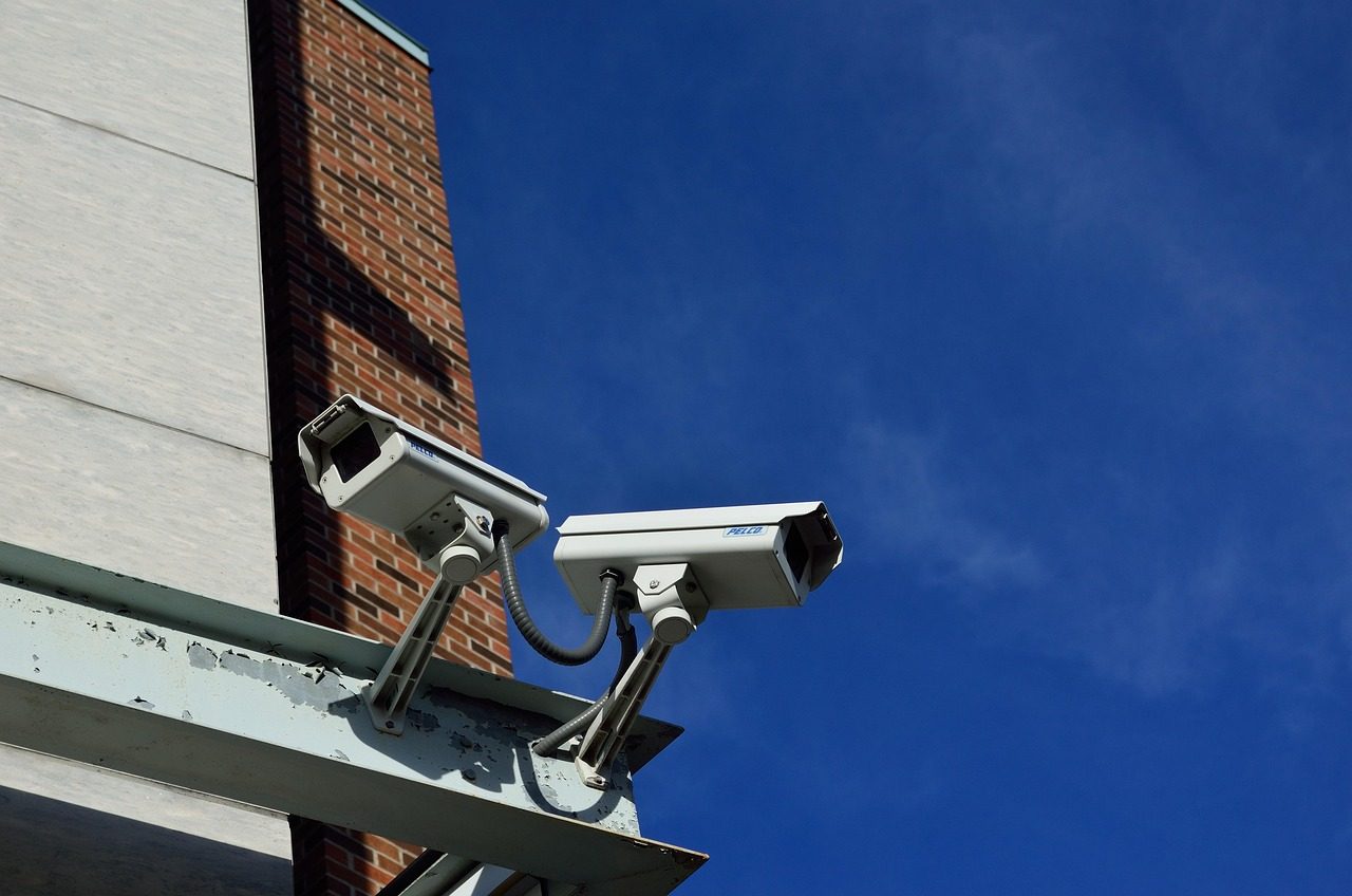 Duas câmeras de vigilância urbana instaladas no alto de um prédio, contra o céu azul